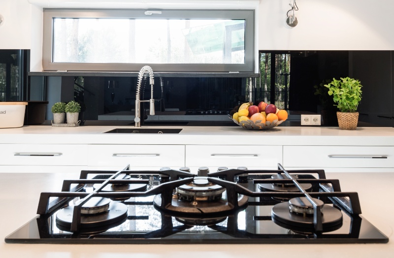 A black kitchen glass splashback with gas stovetop in the foreground